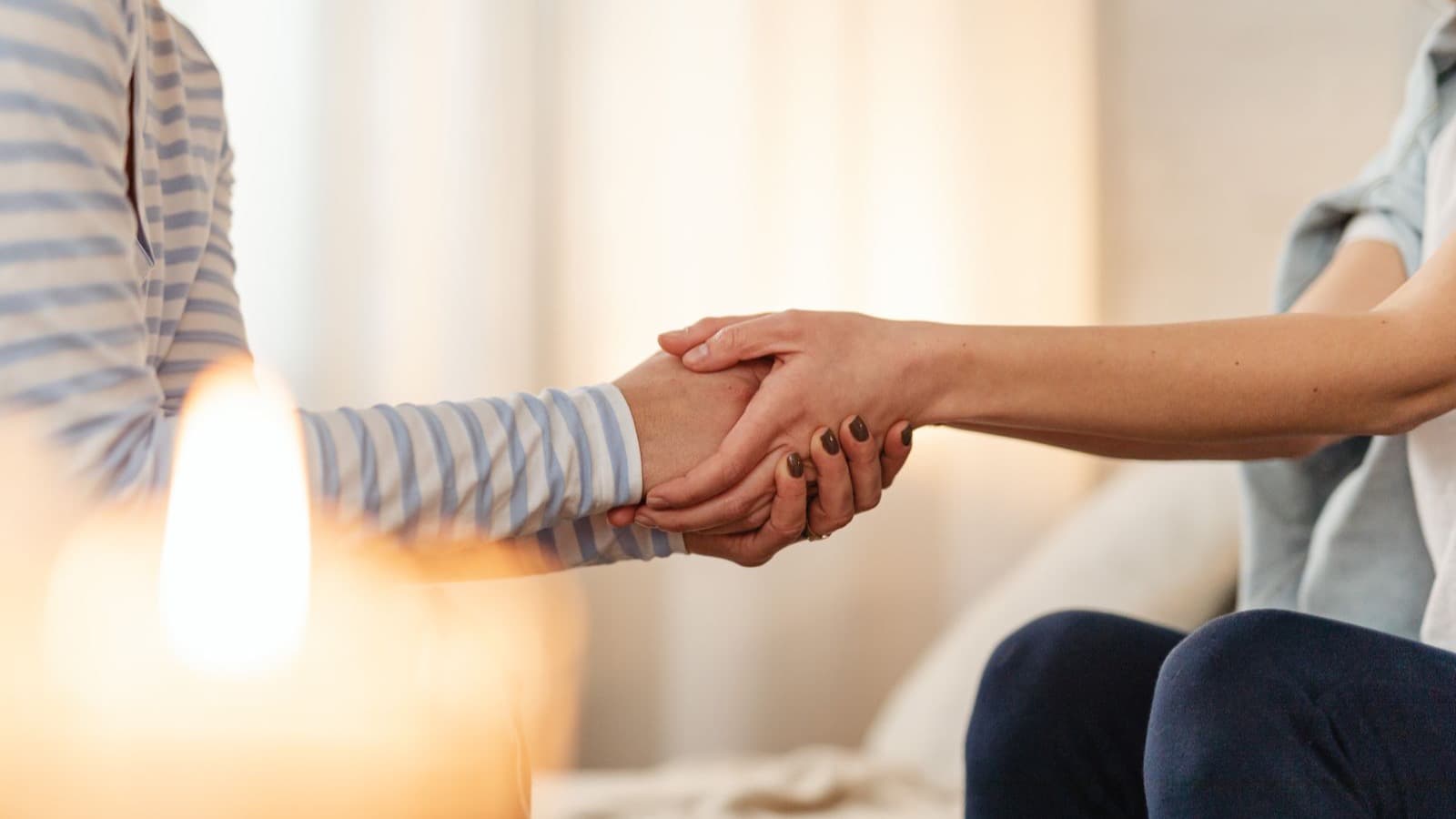 Duas mãos que se seguram em conforto, à luz de uma vela