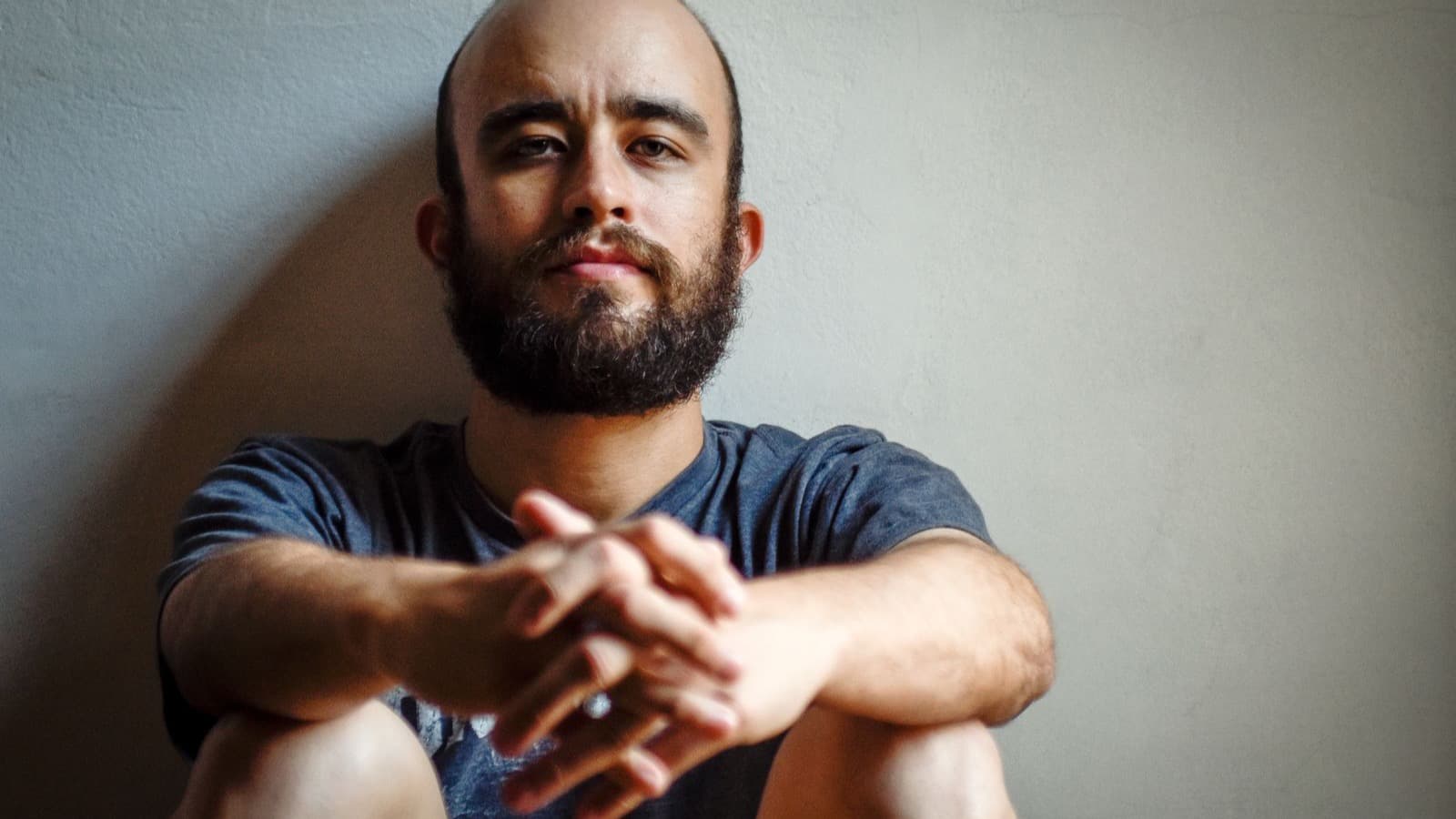 Homem de barba com as mãos entrelaçadas e olhar sereno