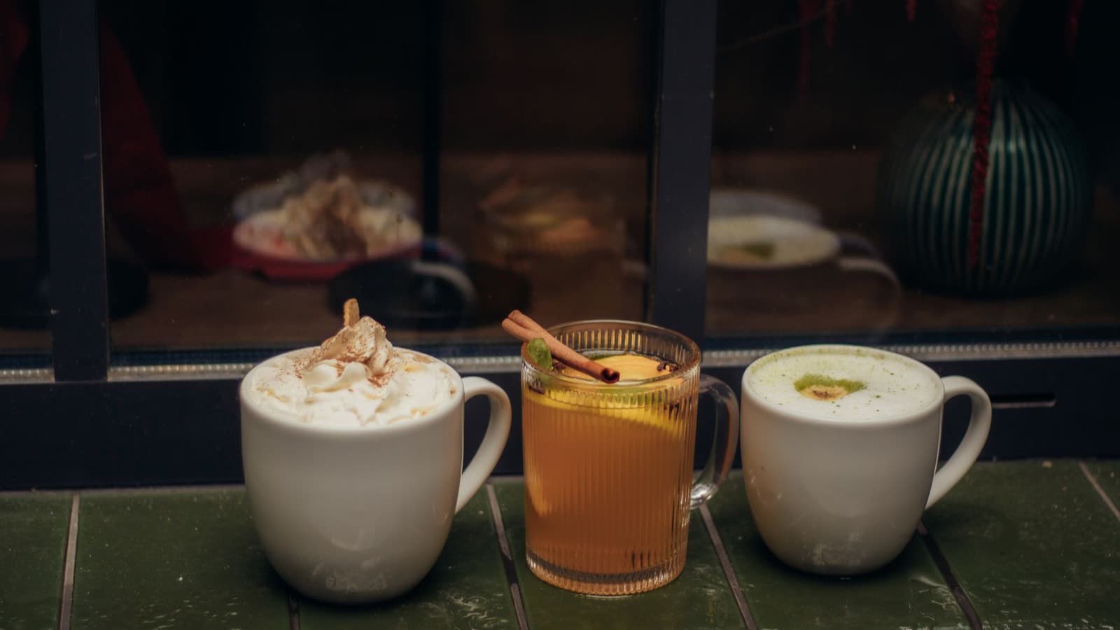 Três bebidas quentes diferentes lado a lado numa mesa junto à janela