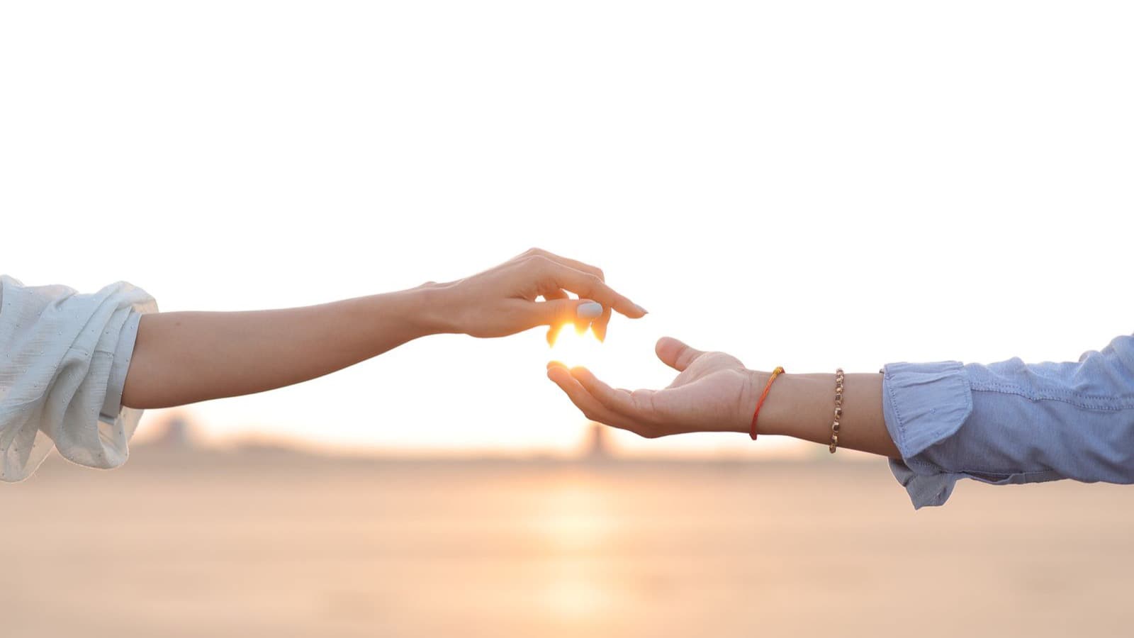 Duas mãos se alcançando ao pôr do sol, com um brilho de luz quente