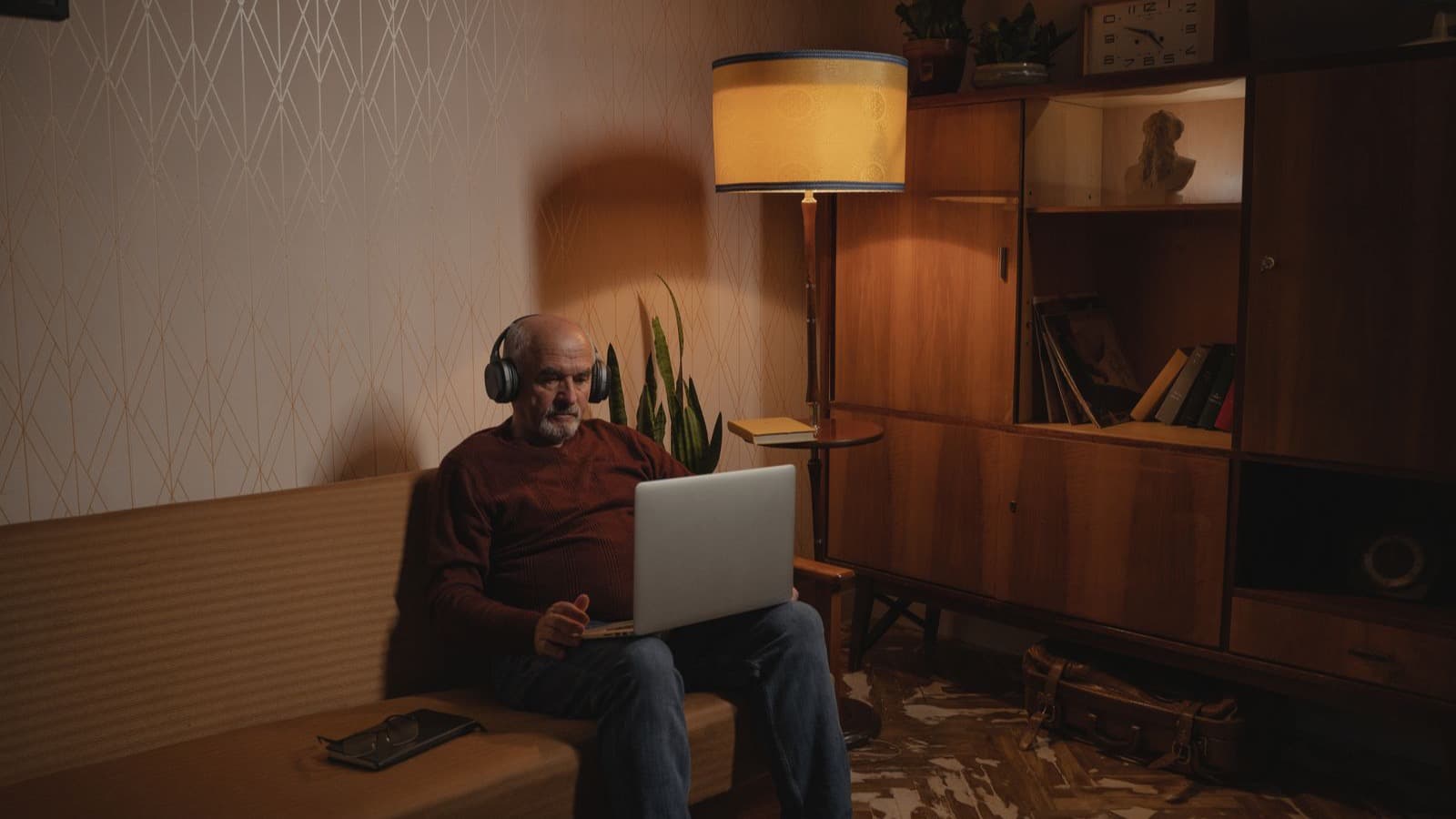 Homem mais velho de fones de ouvido no laptop, em sala aconchegante
